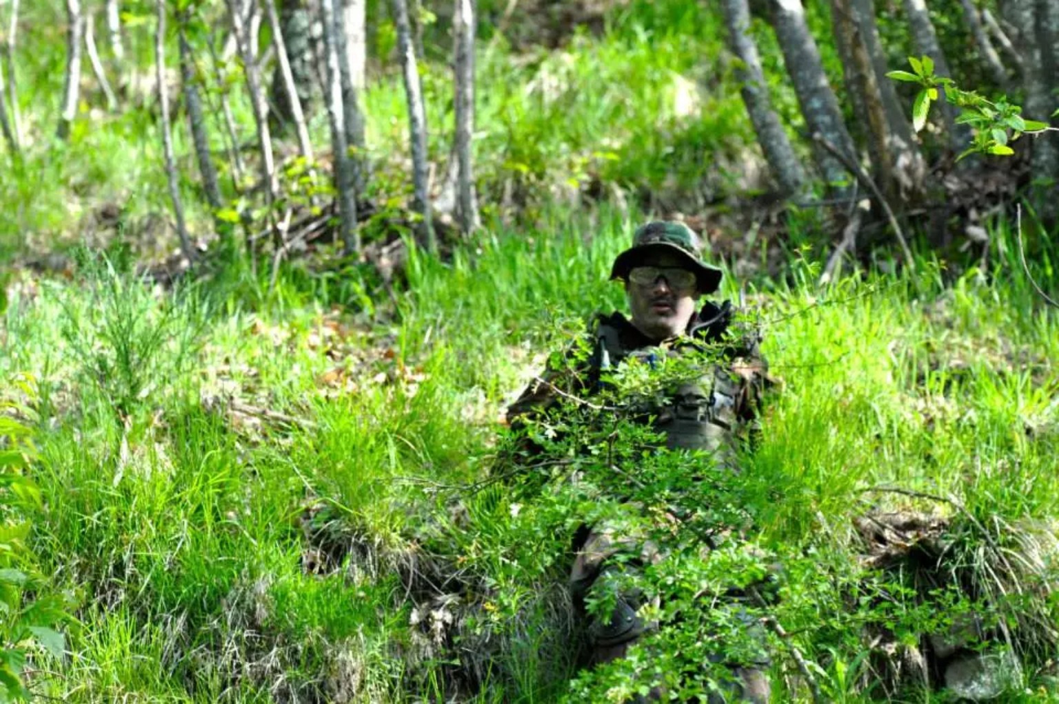 Giocatore softair parzialmente nascosto tra erba e arbusti del bosco