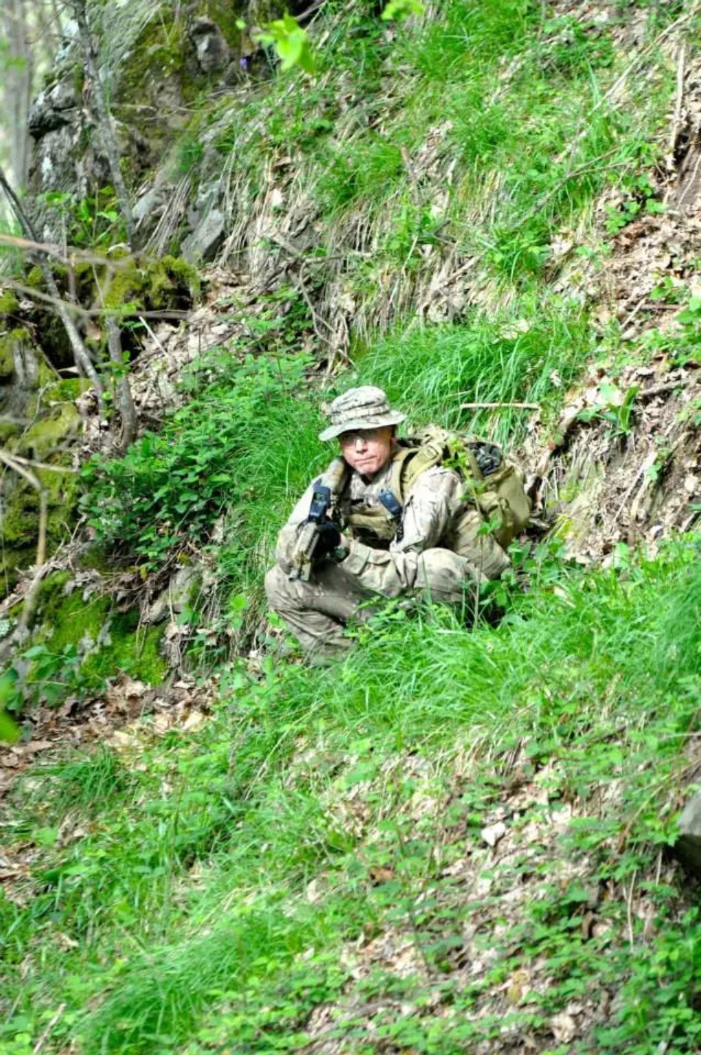 Giocatore softair in posizione nel verde di un pendio boschivo